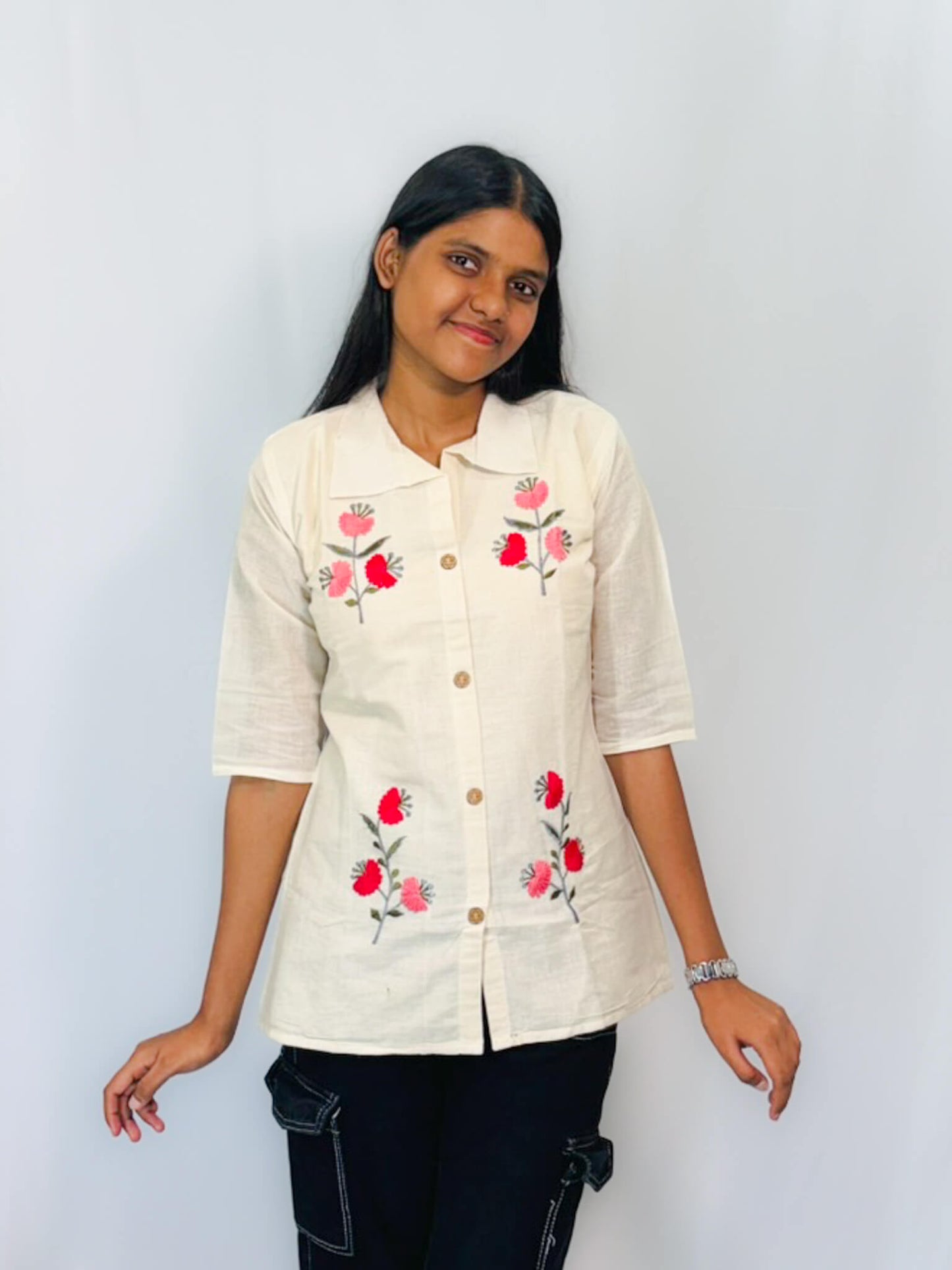 Woman wearing a beige shirt with floral embroidery against a plain background