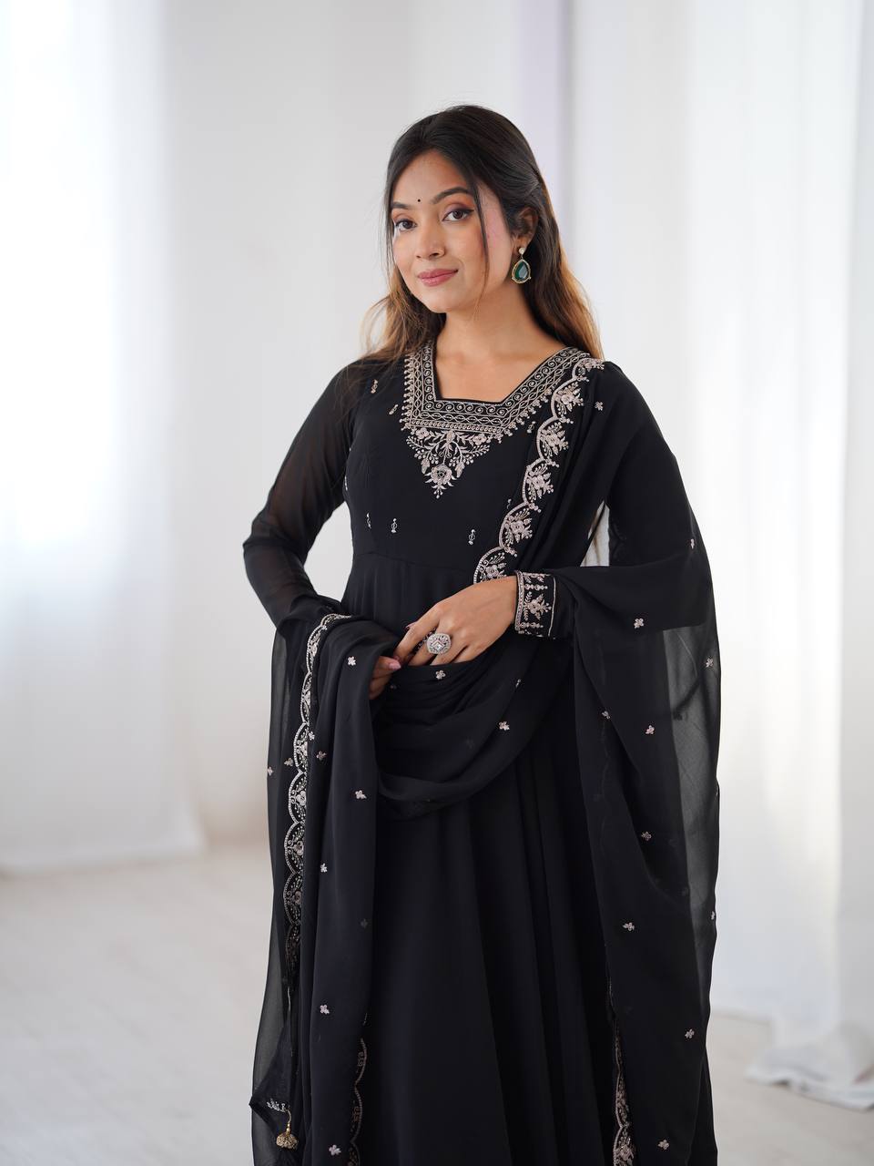 Woman wearing a black traditional outfit with silver embroidery in a bright room.