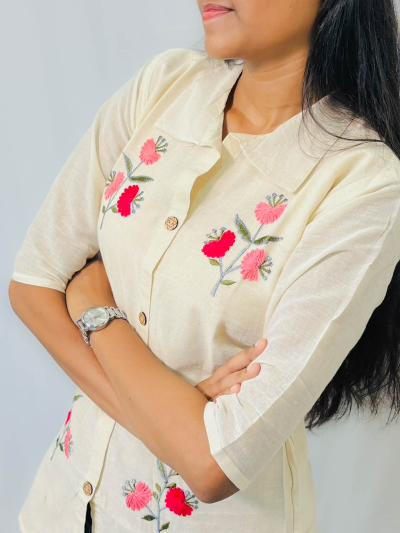 Woman wearing a cream-colored blouse with floral embroidery on a plain background