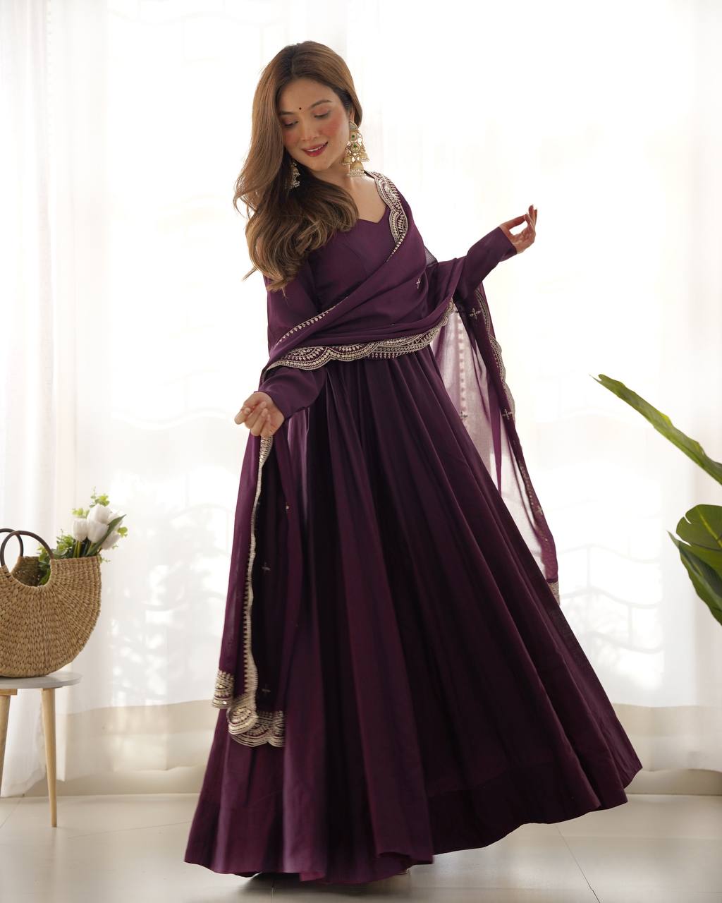 Woman wearing a long purple dress with decorative elements in a bright room.