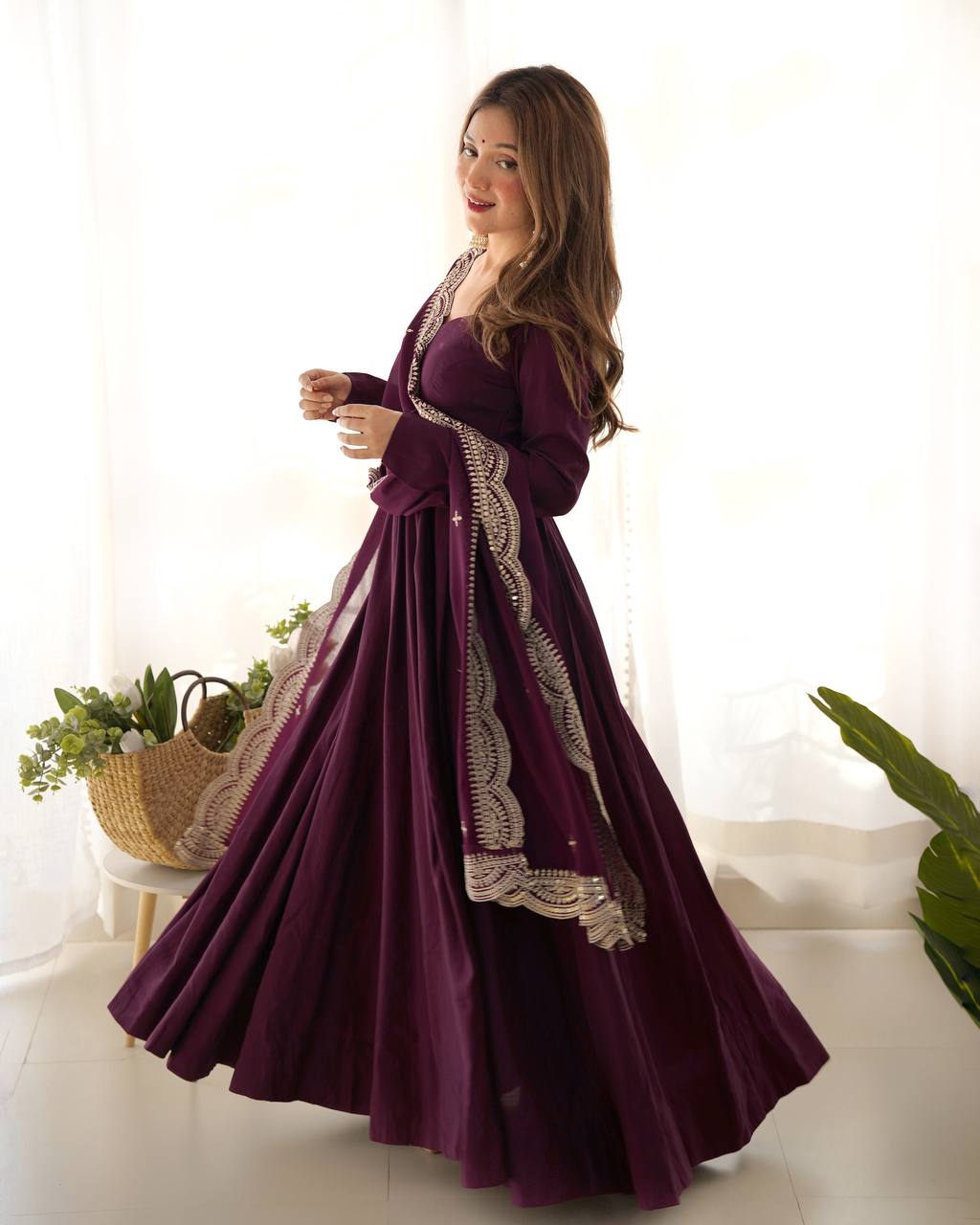 Woman wearing a long purple dress with lace details in a bright room.