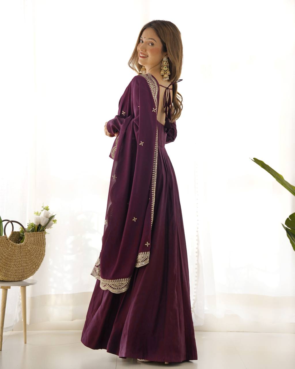 Woman wearing a long purple dress with lace details in a bright room.
