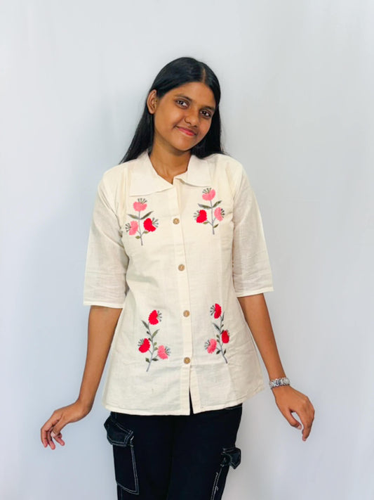 Woman wearing a beige shirt with floral embroidery against a plain background