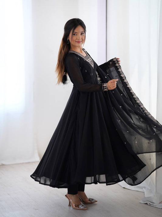 Woman wearing a black traditional outfit with a sheer dupatta in a bright room.