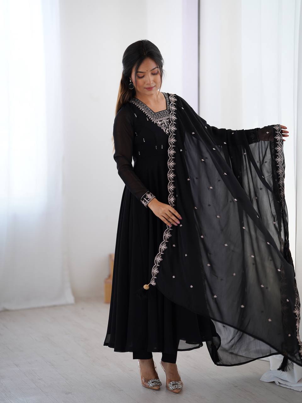 Woman wearing a black traditional outfit with silver embroidery in a bright room.