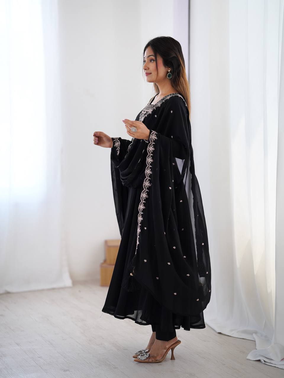 Woman wearing a black dress with white embroidery in a white room