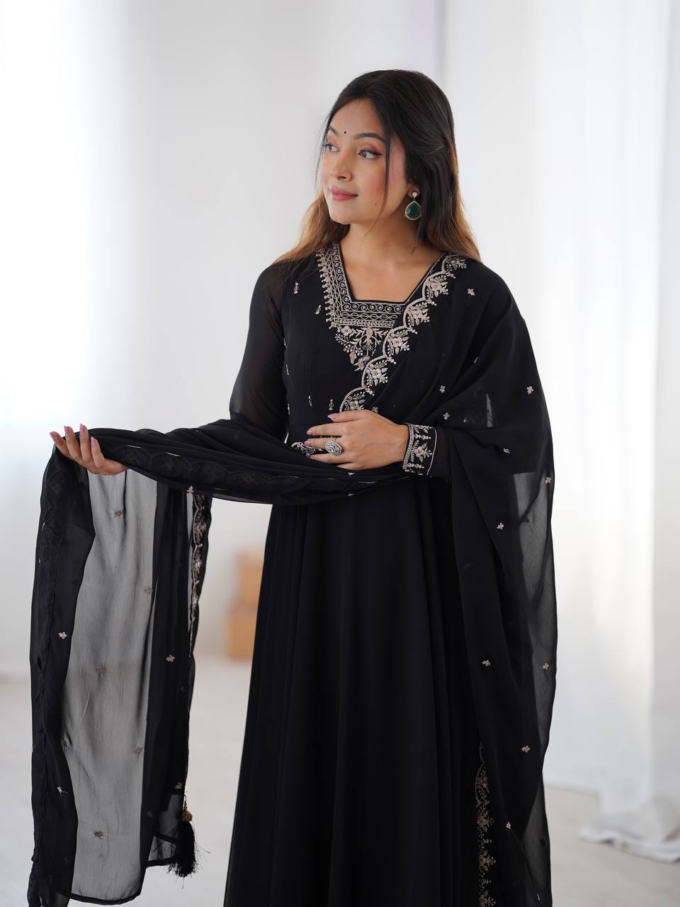 Woman wearing a black dress with intricate silver embroidery against a white background