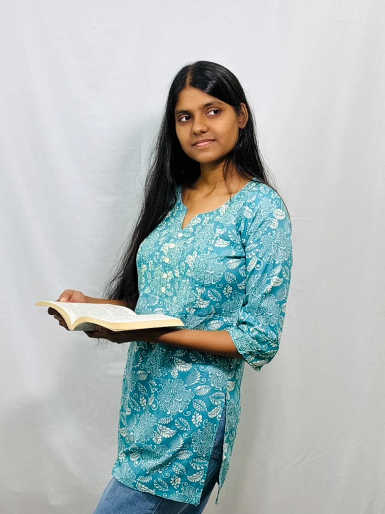 Woman in a blue floral top holding an open book against a plain background