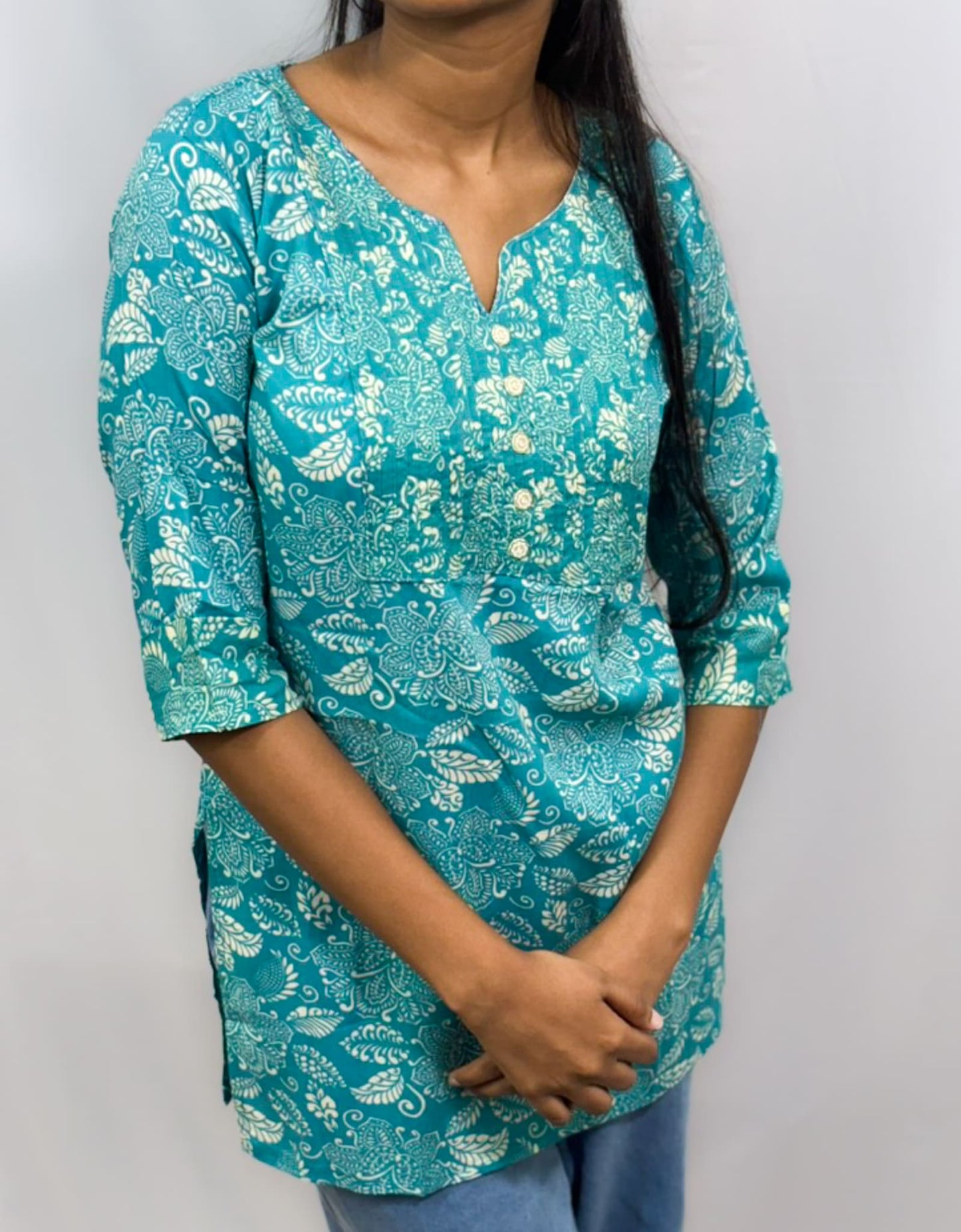 Teal floral patterned top worn by a person on a plain background