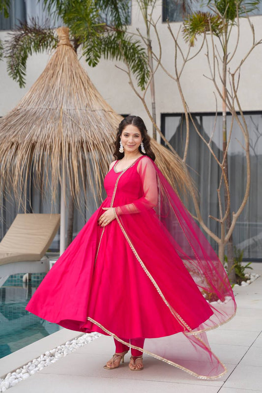 Woman in a bright pink traditional outfit standing by a poolside with plants in the background