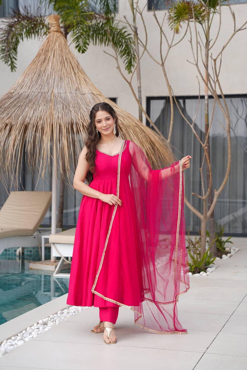 Woman in a pink traditional outfit standing by a poolside with plants in the background