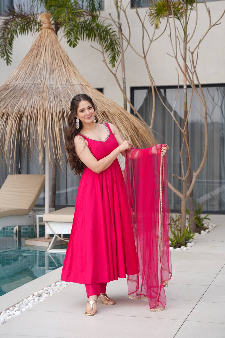 Woman in a pink traditional outfit holding a dupatta by a poolside.