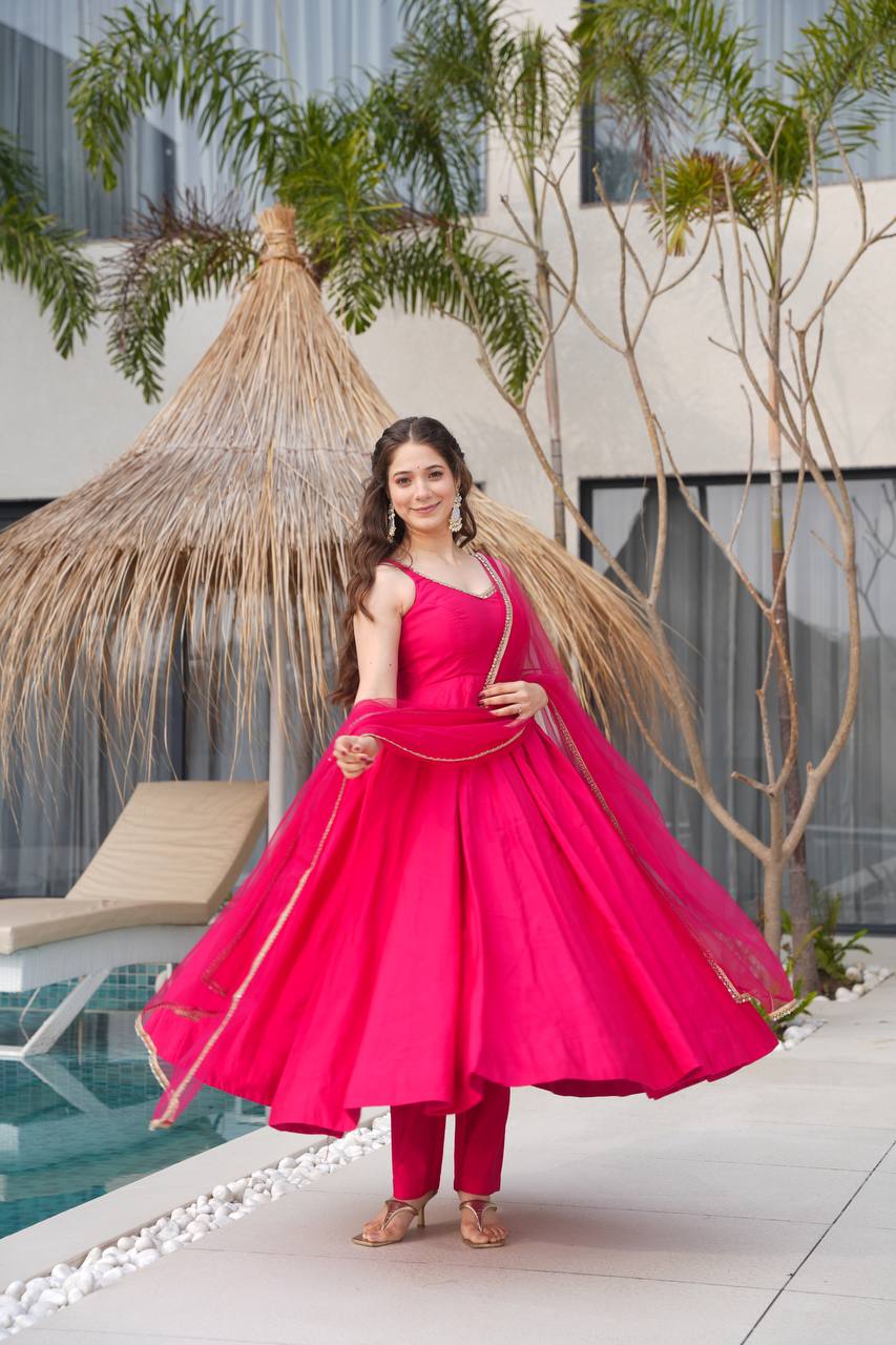 Woman in a bright pink traditional outfit standing by a poolside with greenery in the background