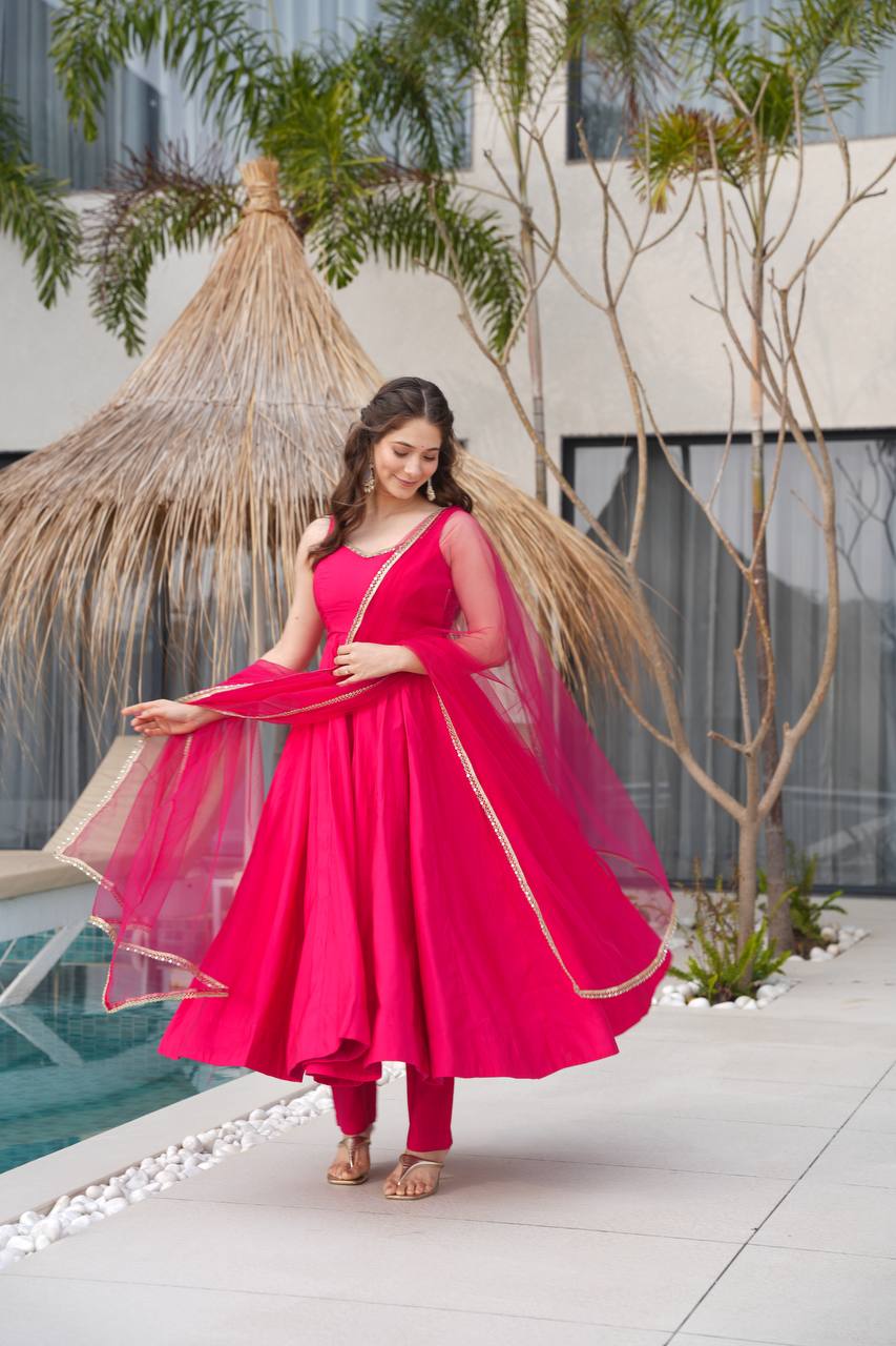 Woman in a bright pink traditional outfit standing by a poolside with plants in the background