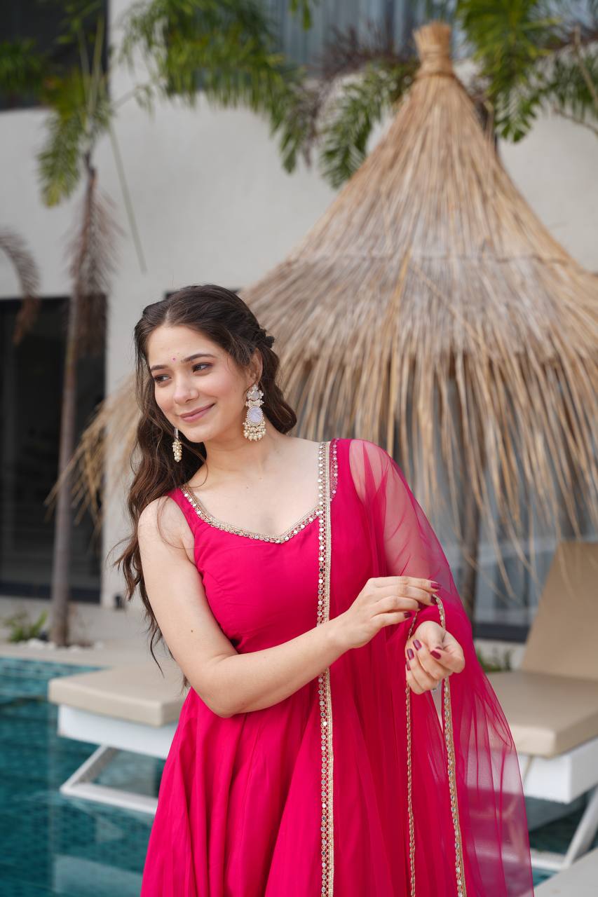 Woman in a pink traditional outfit standing by a poolside with plants in the background