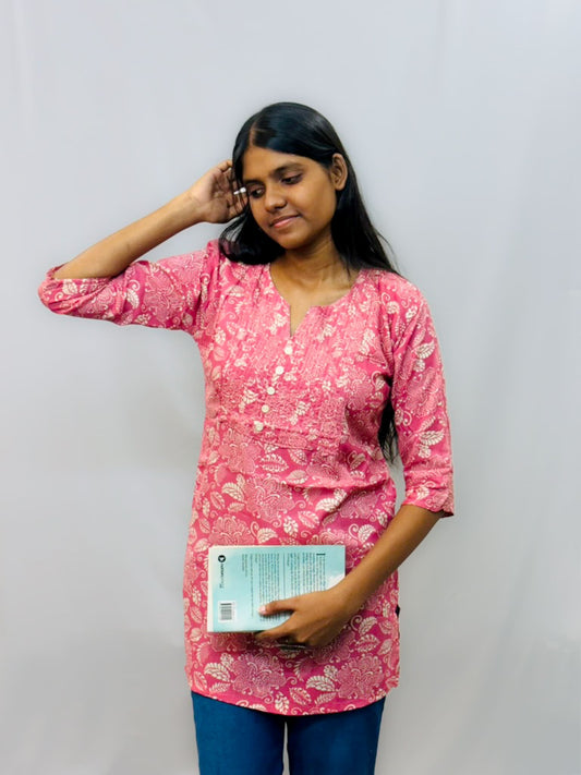Woman wearing a pink floral top holding a book against a plain background