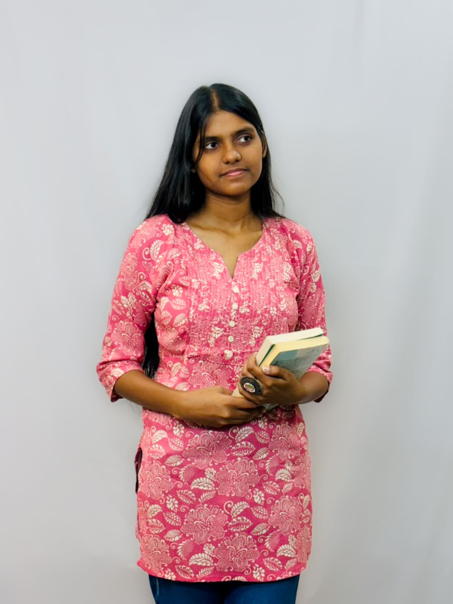 Woman in a pink floral top holding a book against a plain background