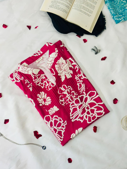 Red fabric with white floral patterns on a white surface with petals and an open book.