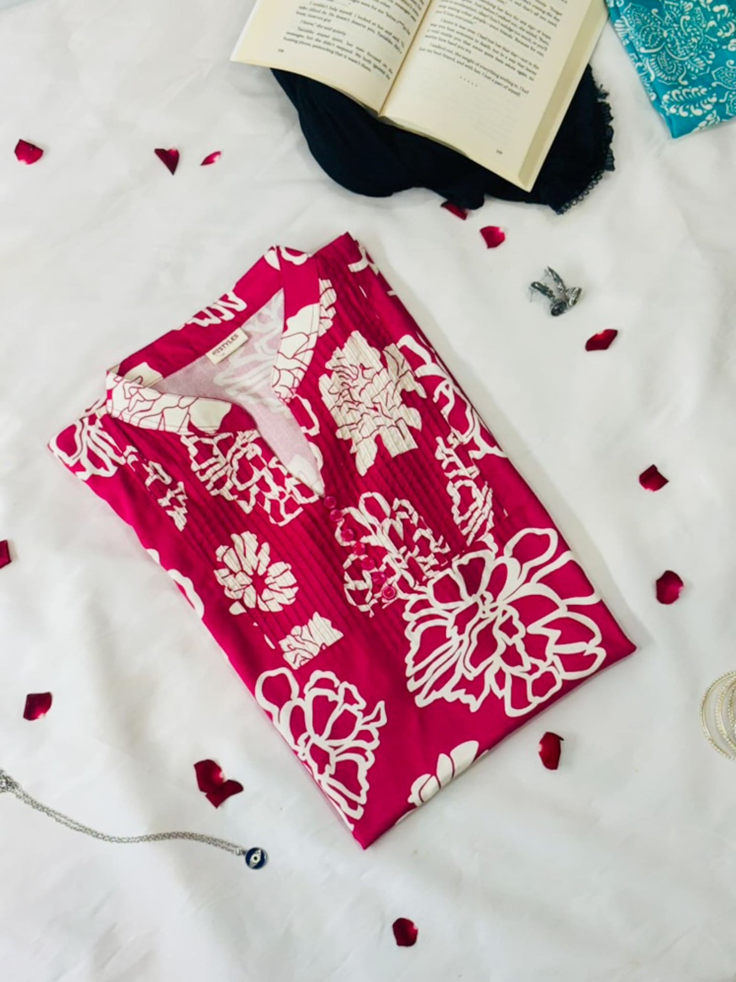 Red fabric with white floral patterns on a white surface with petals and an open book.