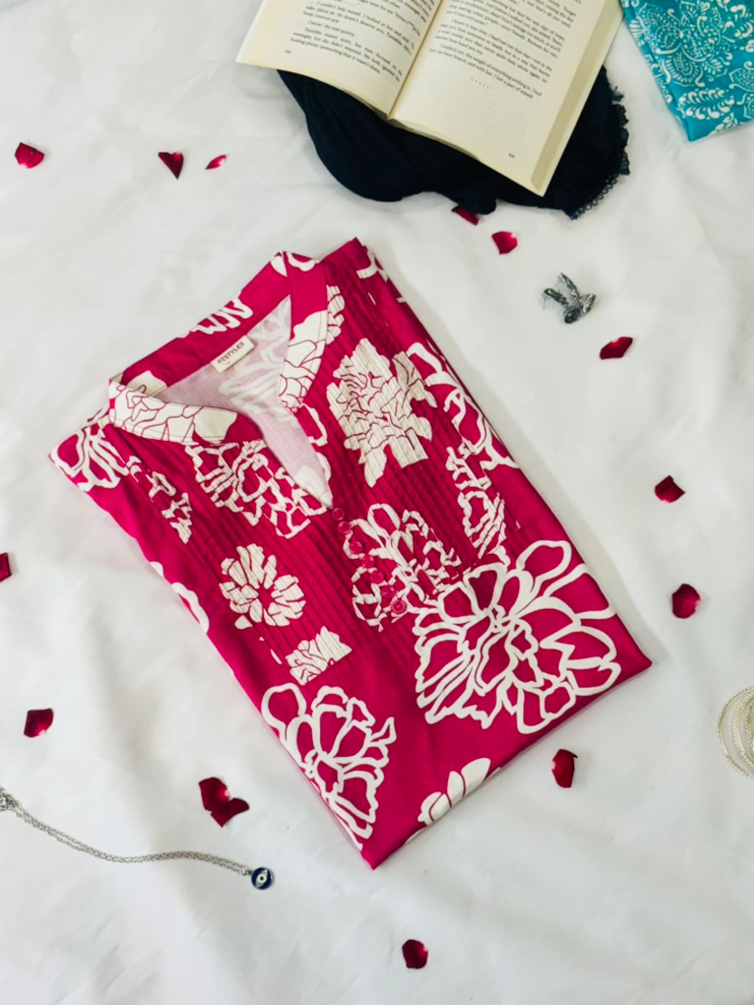 Red fabric with white floral patterns on a white surface with petals and an open book.