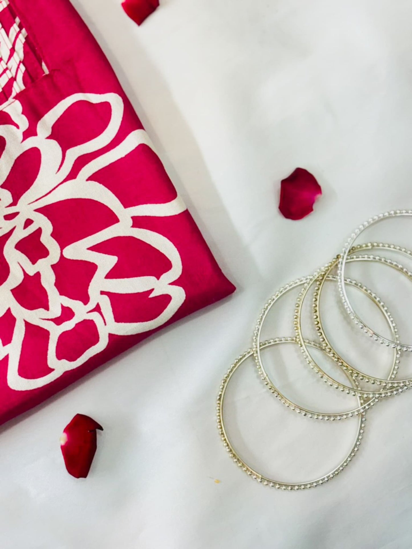 Silver bangles on a white surface with red fabric and rose petals.