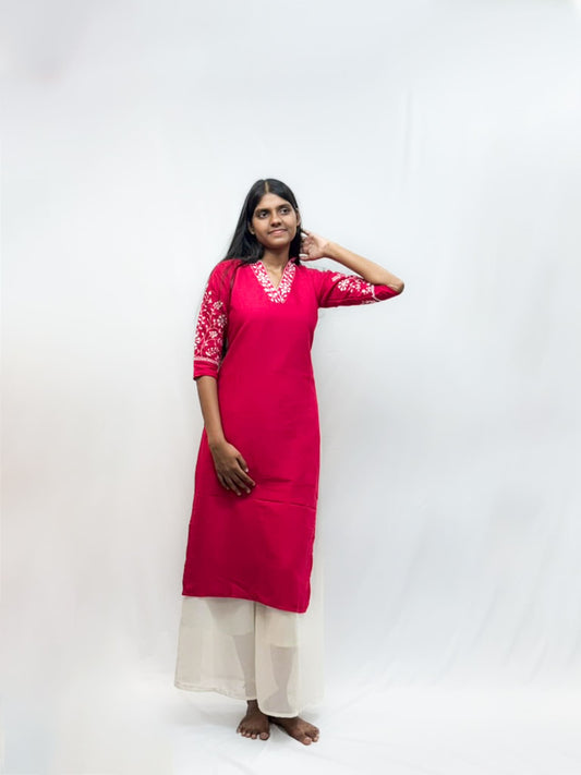 Woman wearing a red kurta with white embroidery on a plain background