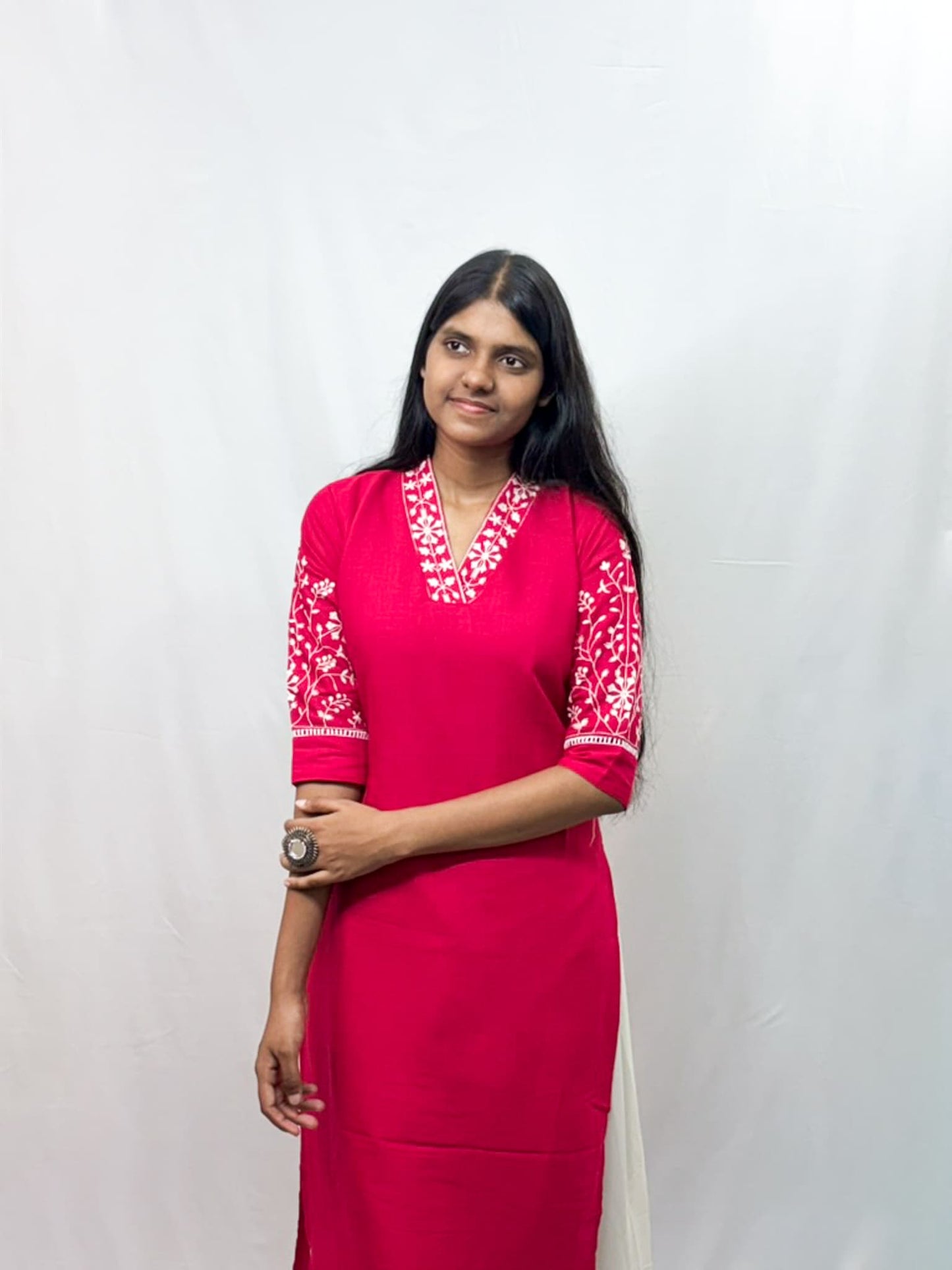 Woman wearing a bright pink traditional outfit with white embroidery on a plain background