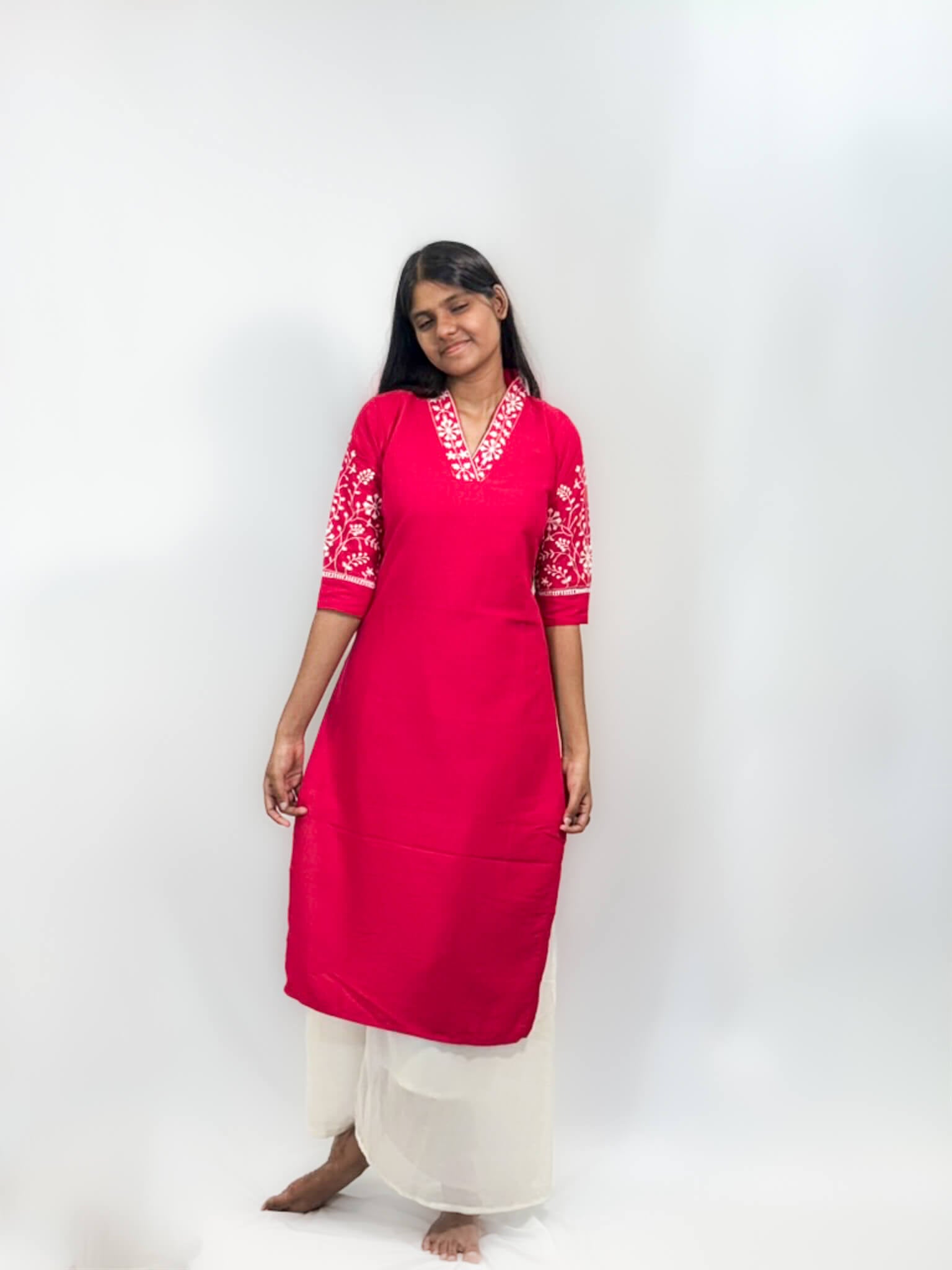 Woman wearing a bright pink kurta with white embroidery on a white background