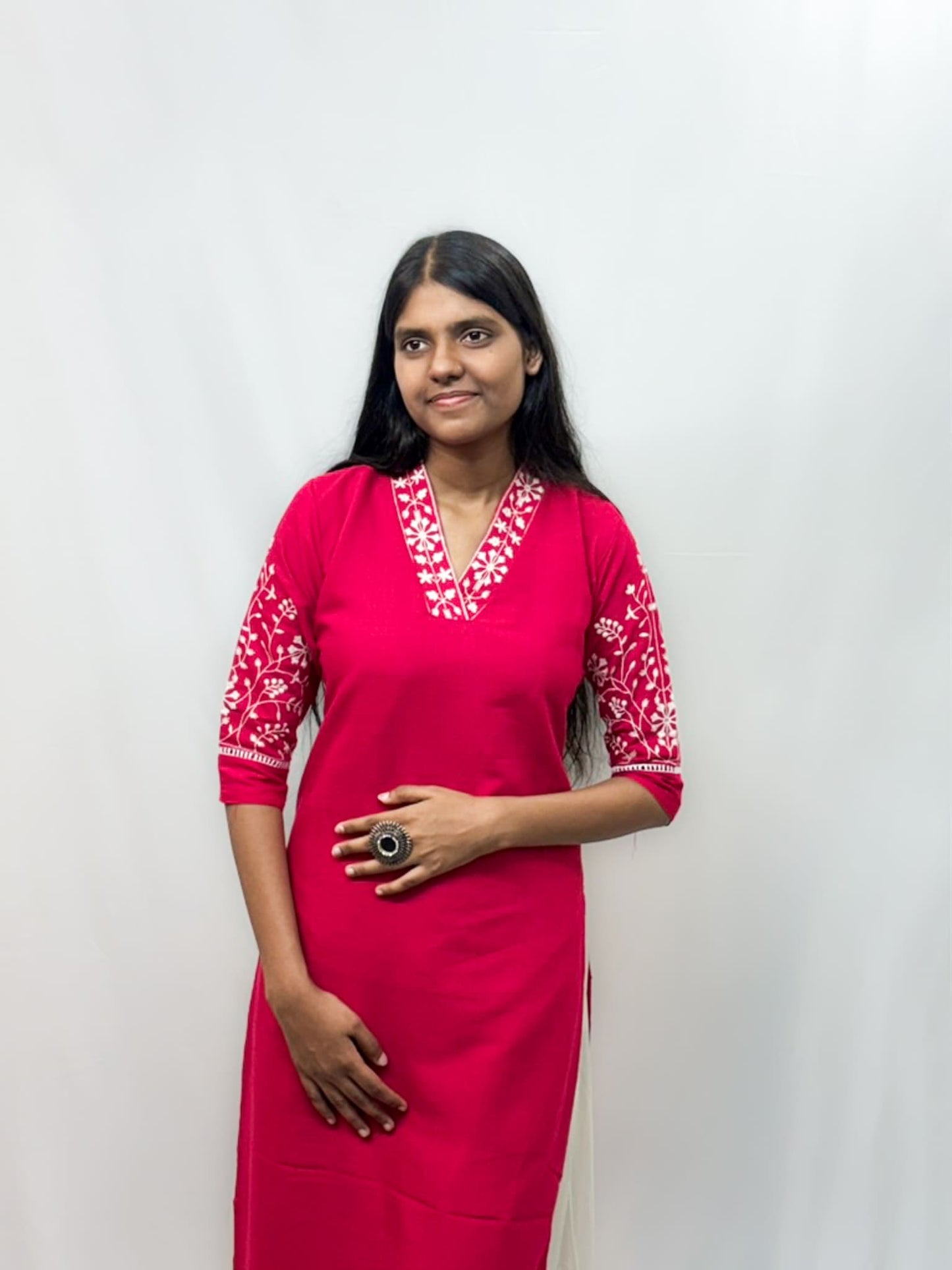 Woman wearing a pink dress with white embroidery against a plain background