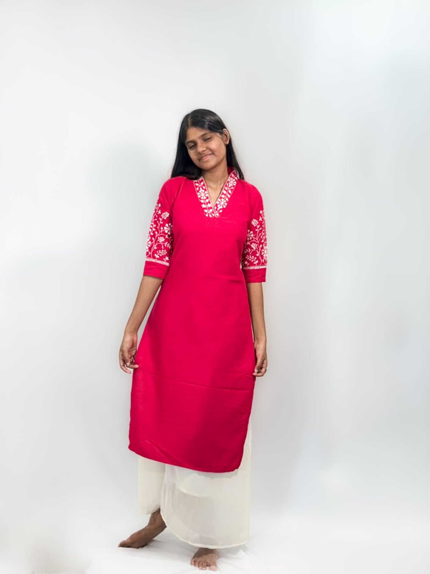 Woman wearing a bright pink kurta with white embroidery on a white background