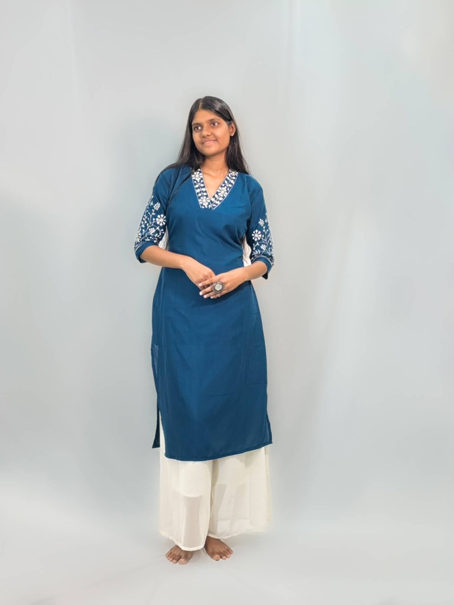 Woman wearing a blue kurta with white embroidery on a plain background