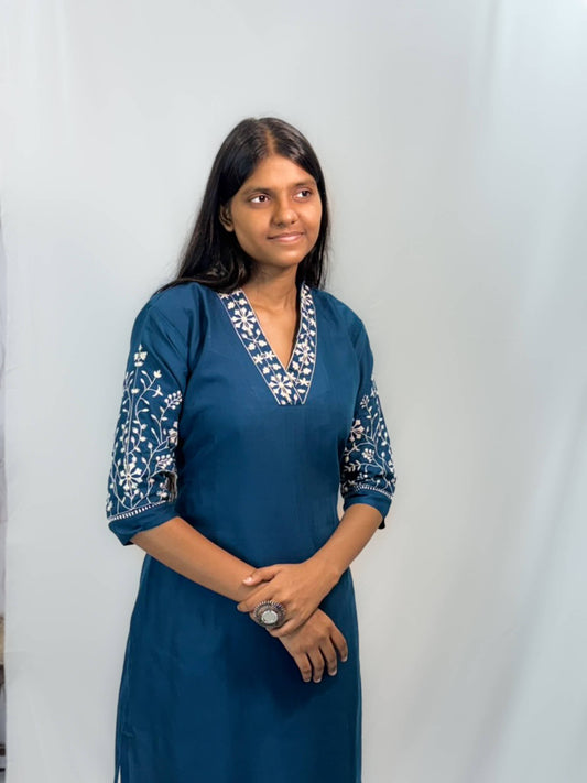 Woman wearing a blue dress with white patterns against a plain background