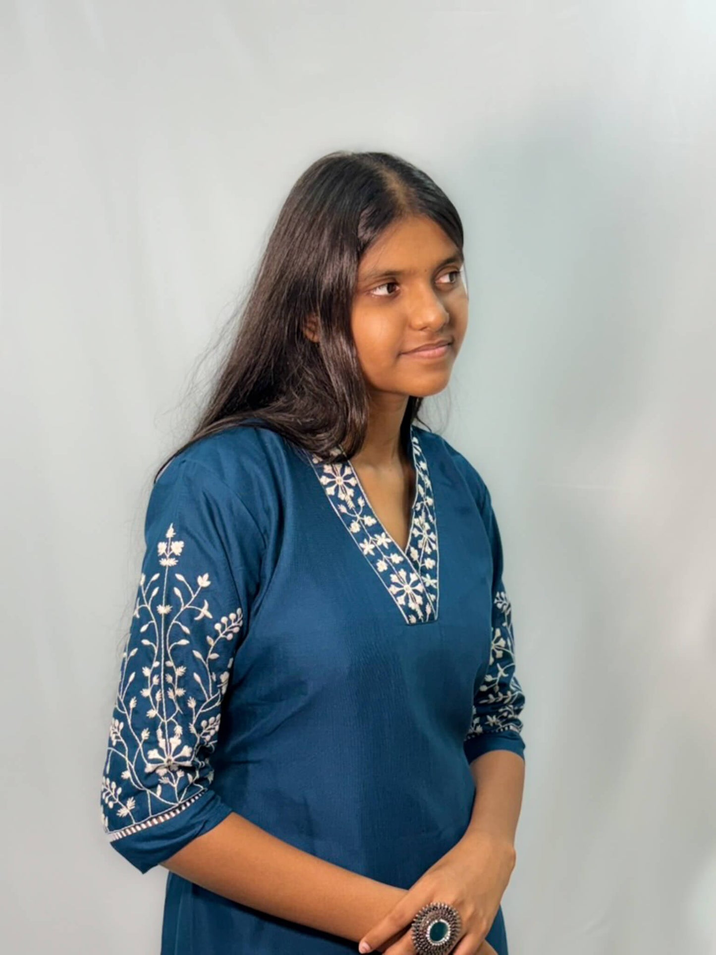 Woman wearing a blue embroidered top against a plain background