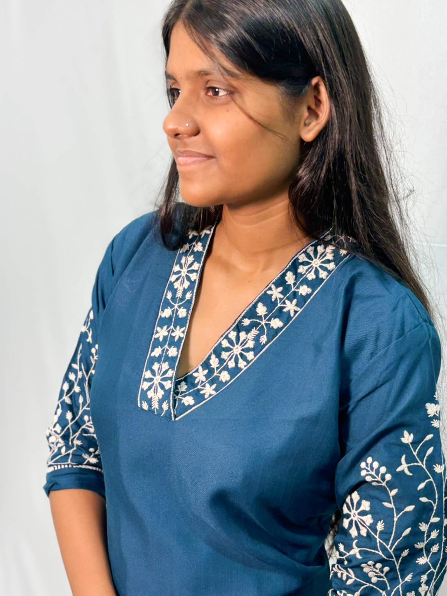 Woman wearing a blue kurta with white embroidery against a plain background