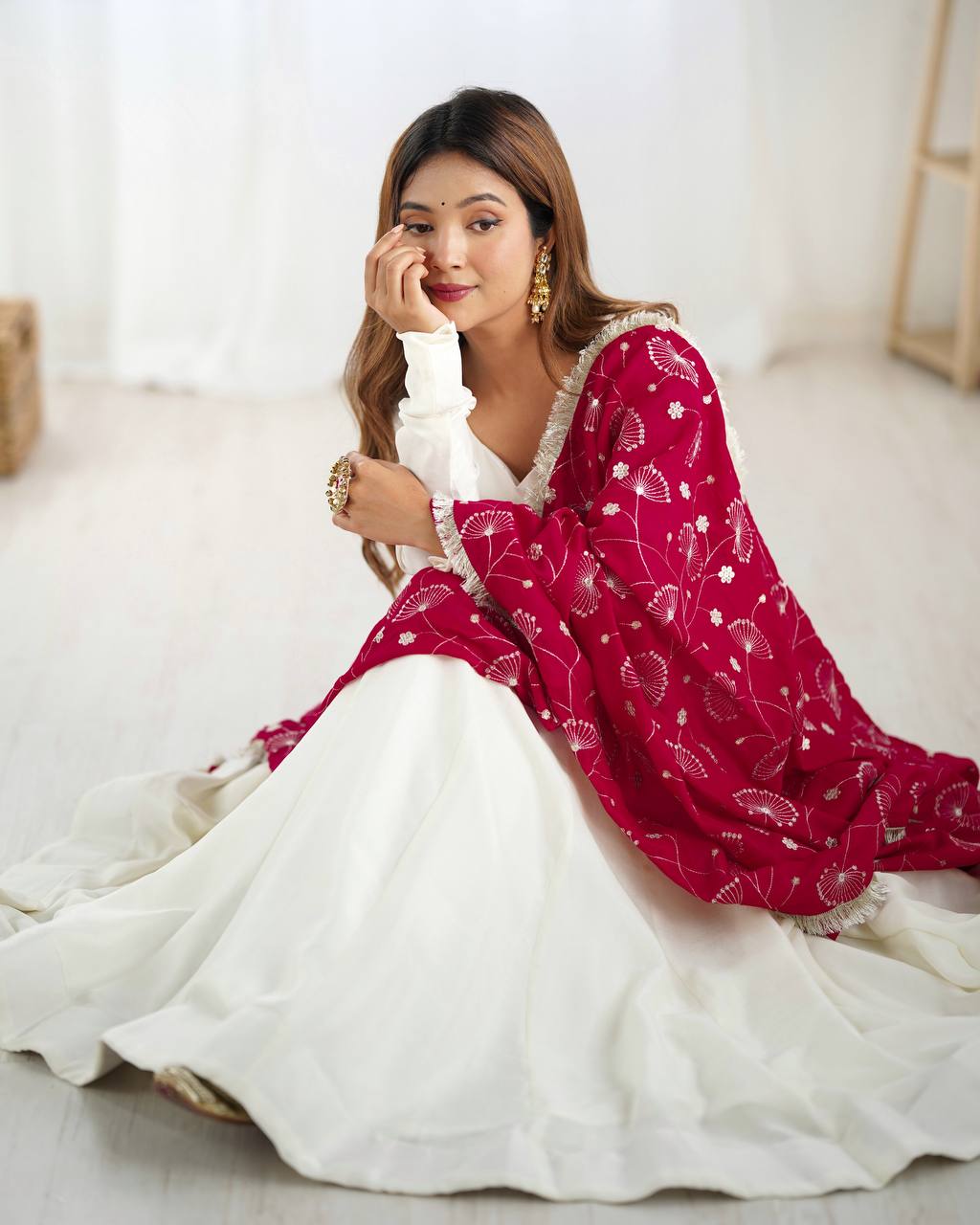 Woman in a red and white traditional outfit sitting on a light-colored floor.