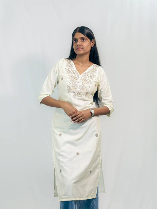 Woman wearing a white traditional outfit with intricate designs against a plain background