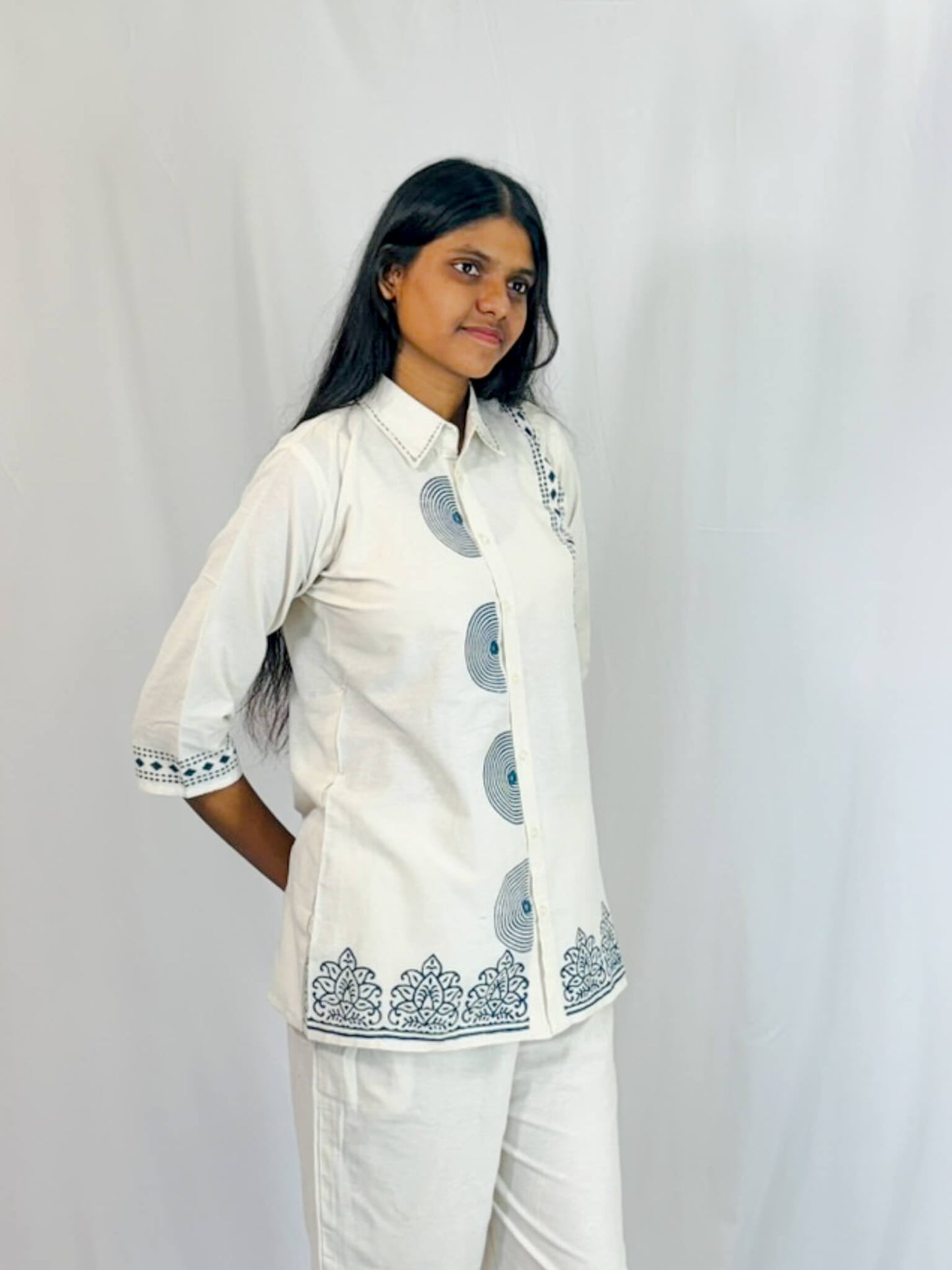 Woman wearing a white traditional outfit with blue patterns on a plain background