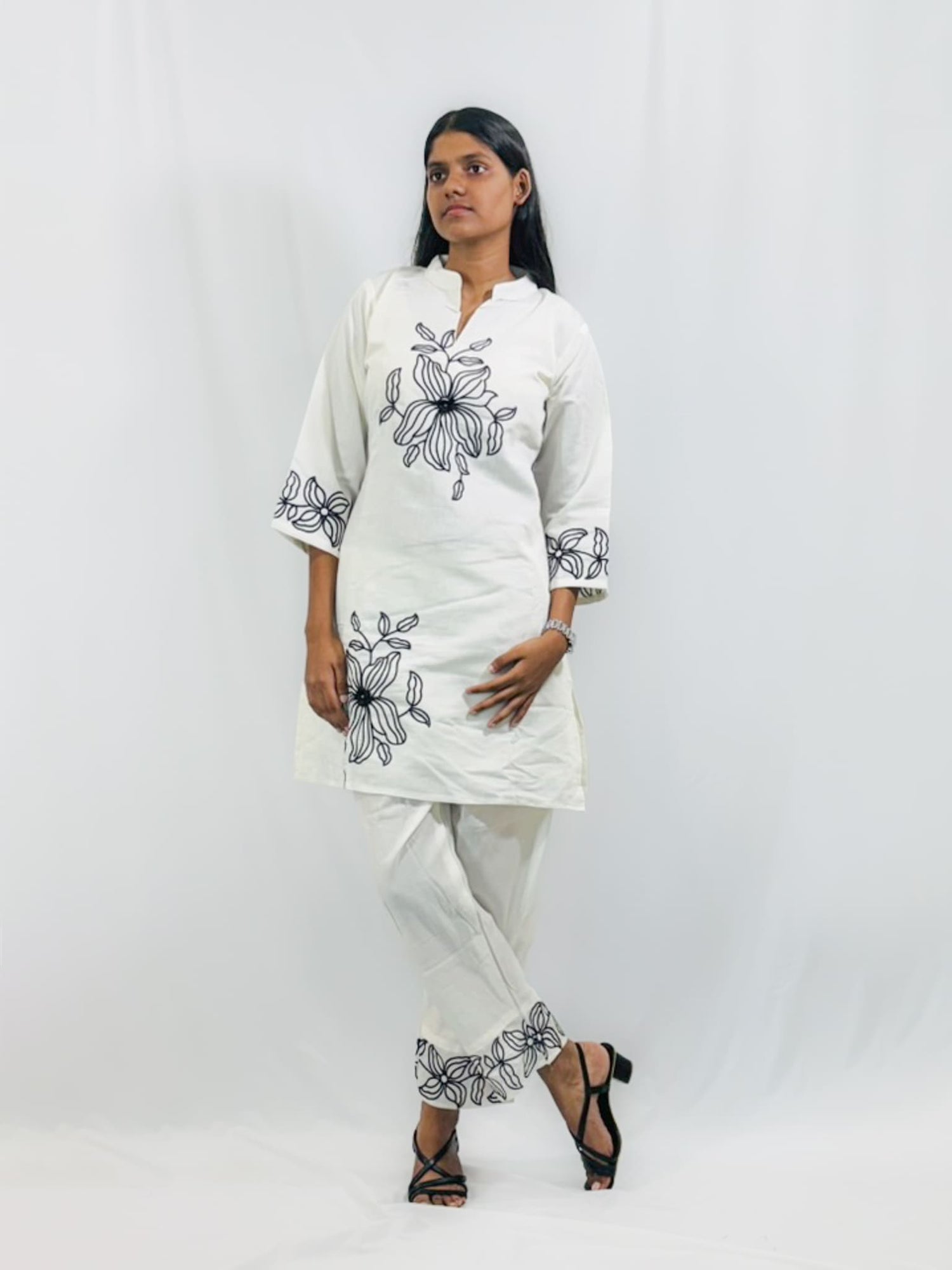 Woman wearing a white kurta with black floral embroidery on a plain background