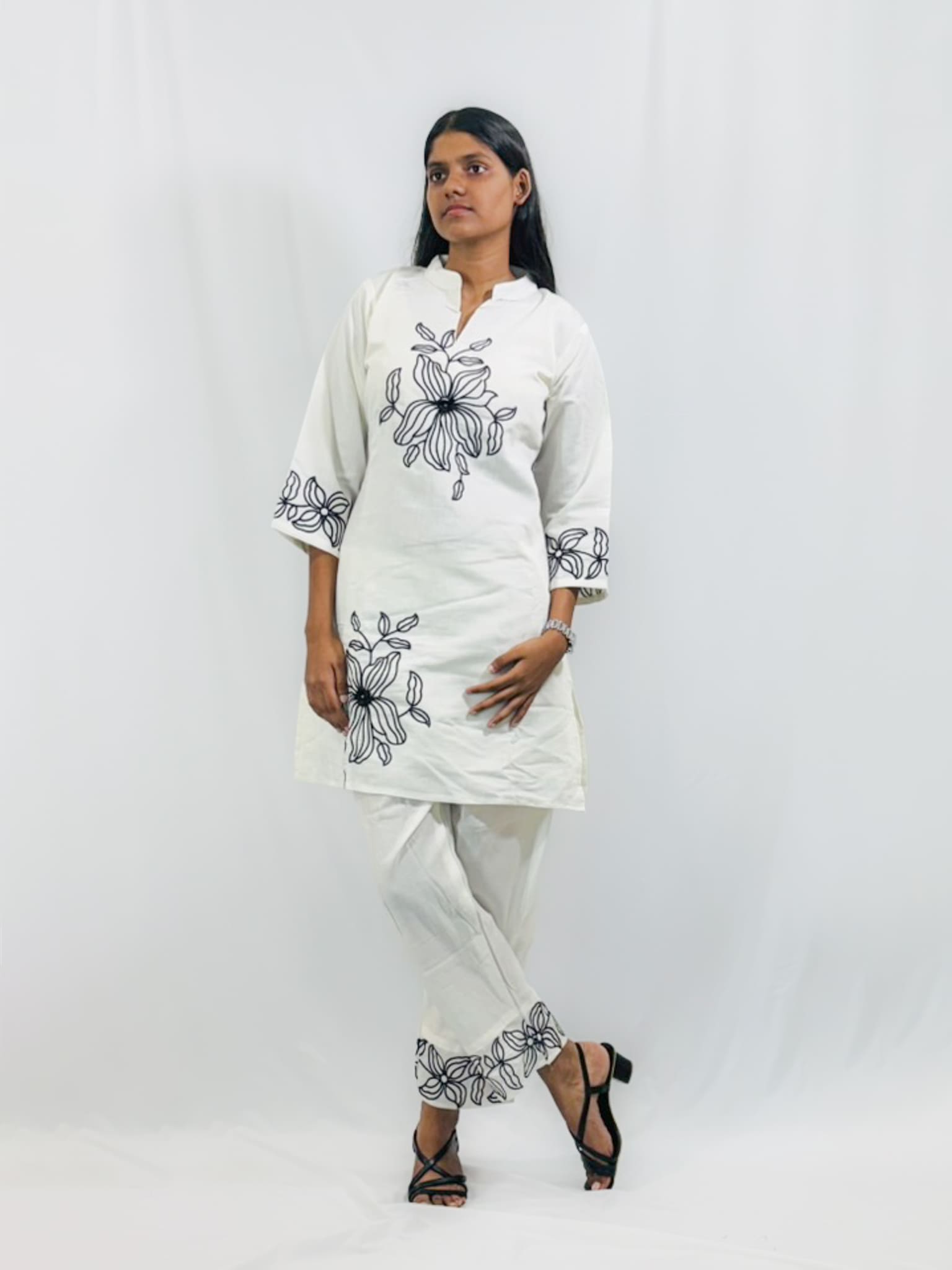 Woman wearing a white kurta with black floral embroidery on a plain background
