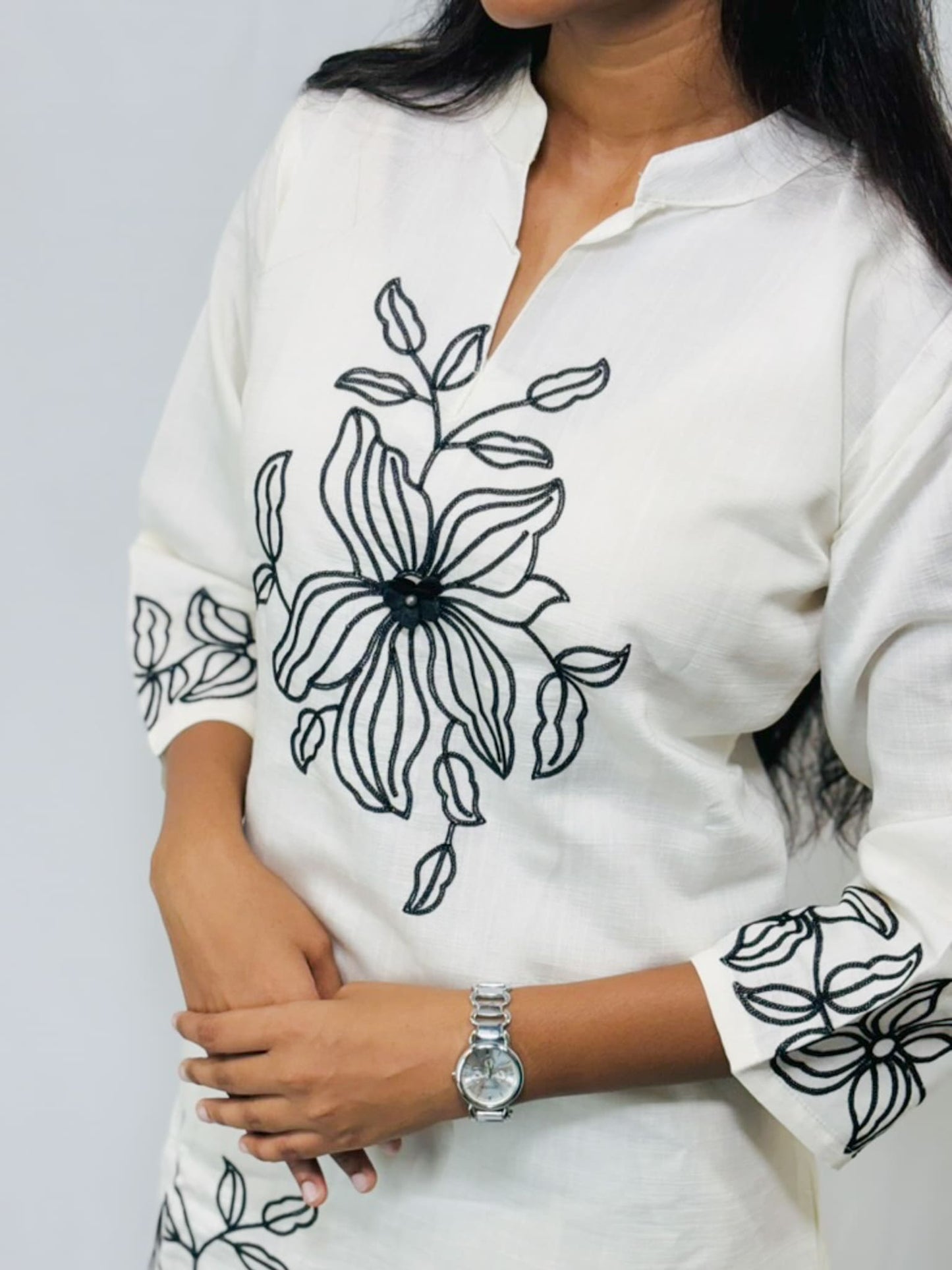 White blouse with black floral embroidery on a plain background