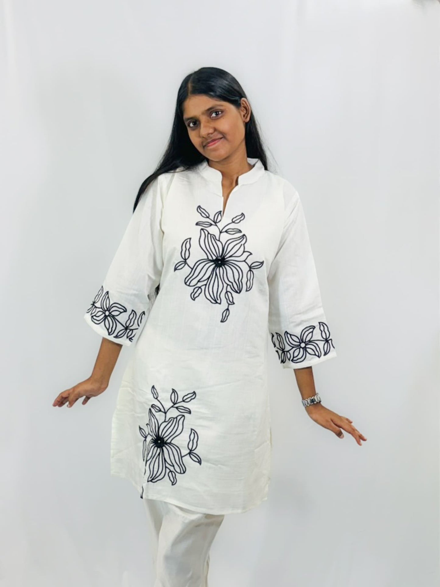 Woman wearing a white kurta with black floral embroidery on a plain background