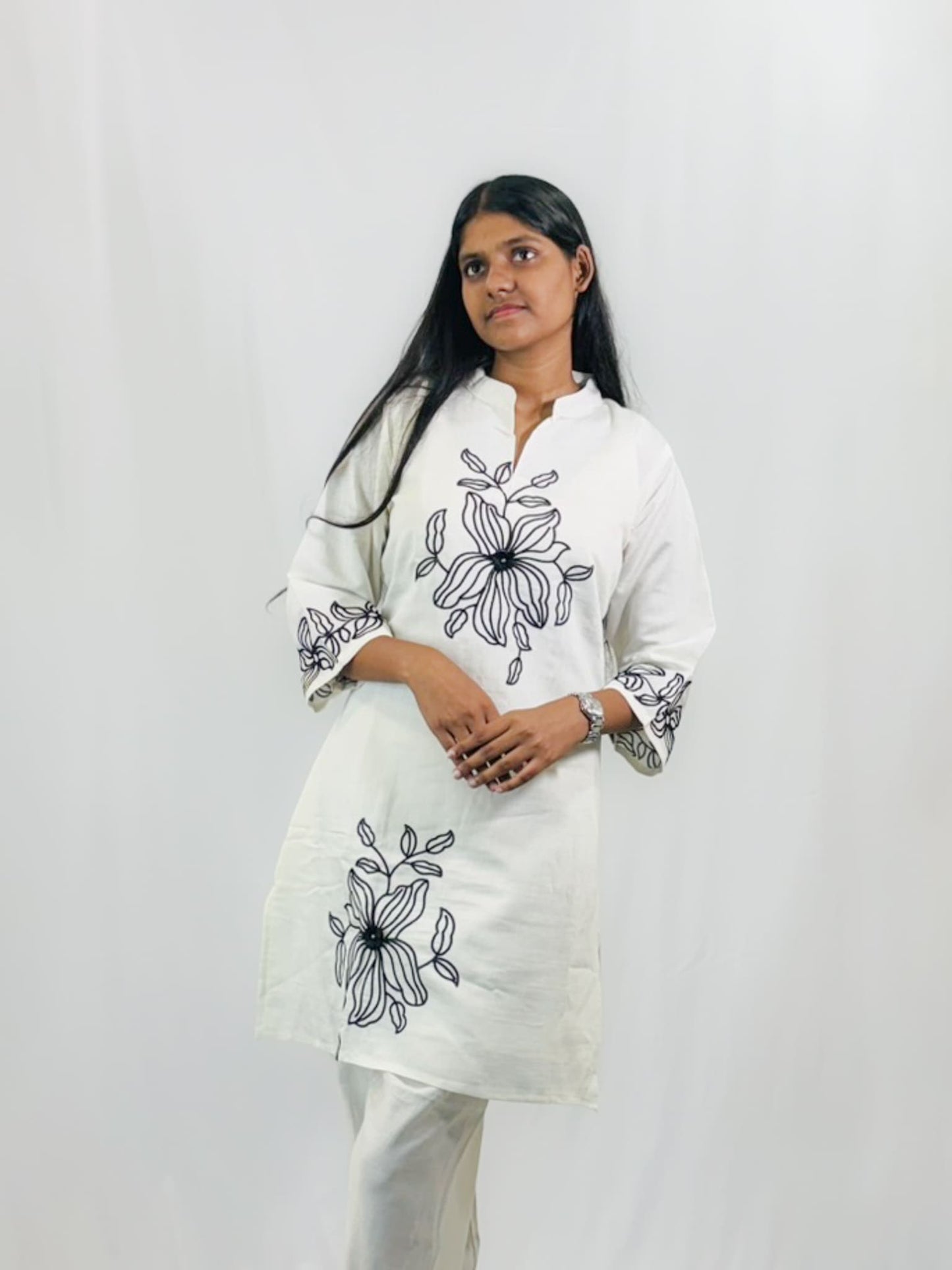 Woman wearing a white kurta with black floral embroidery on a plain background