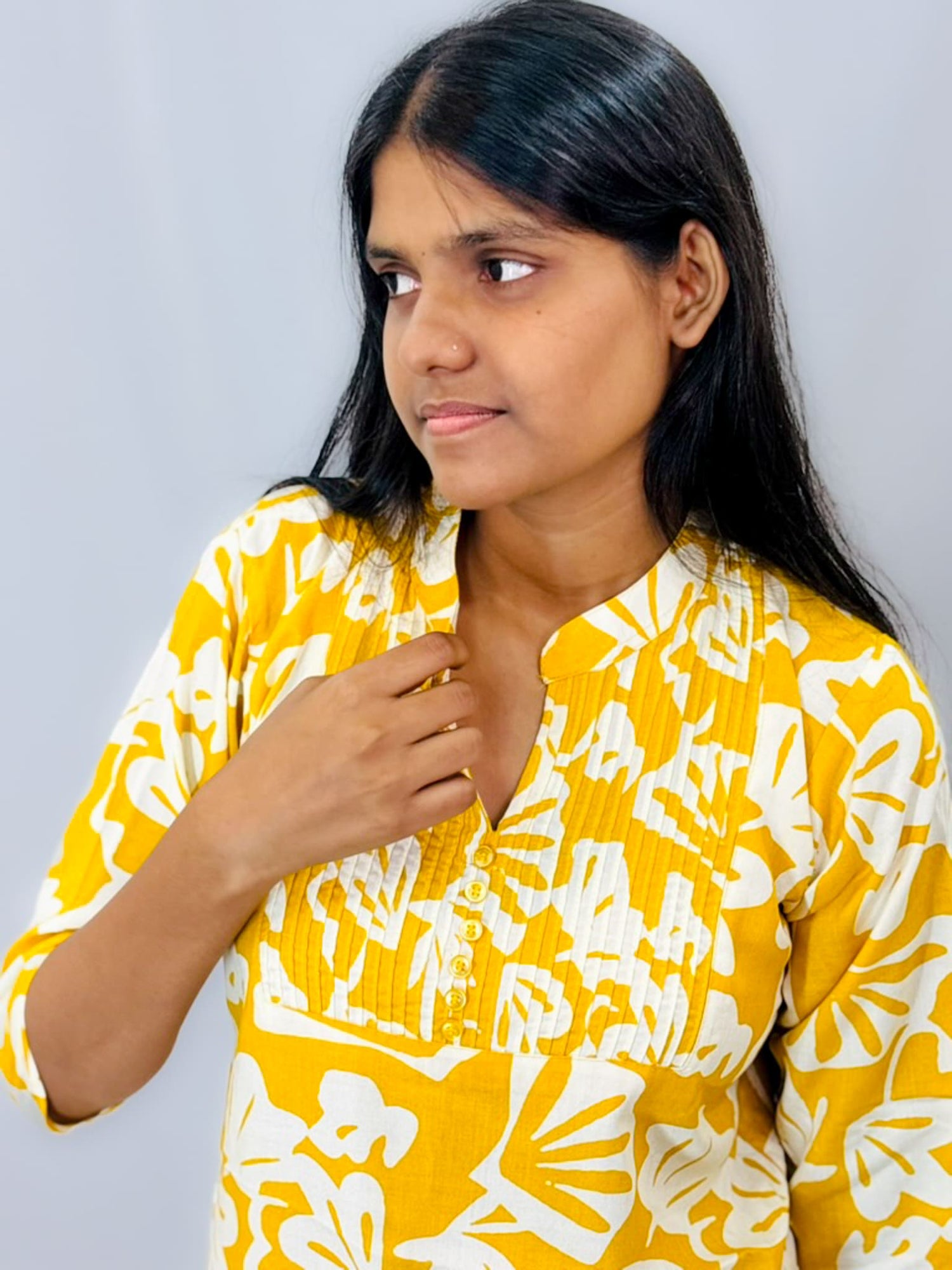 Woman wearing a yellow and white patterned top against a plain background