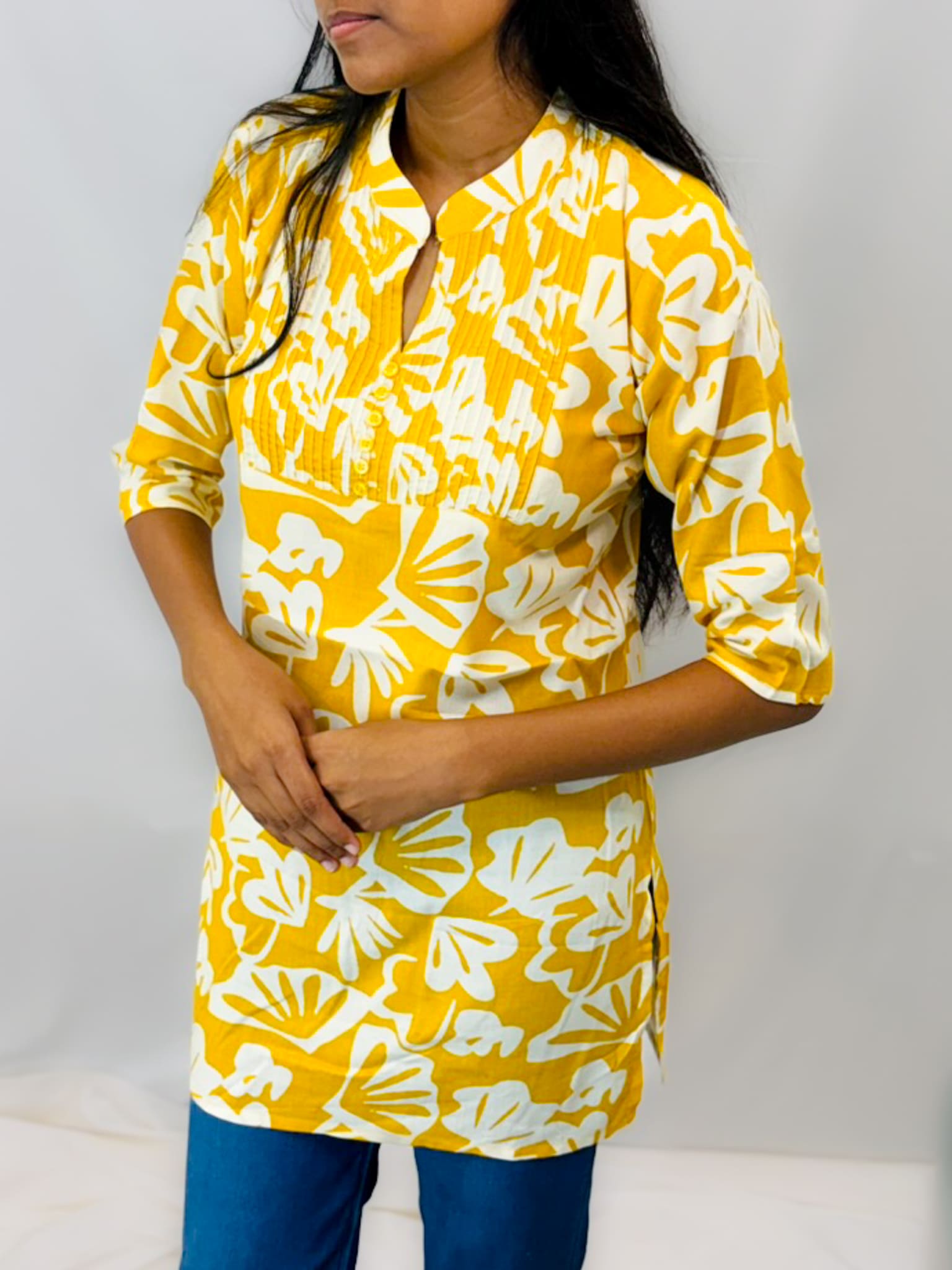 Person wearing a yellow and white floral patterned shirt against a plain background