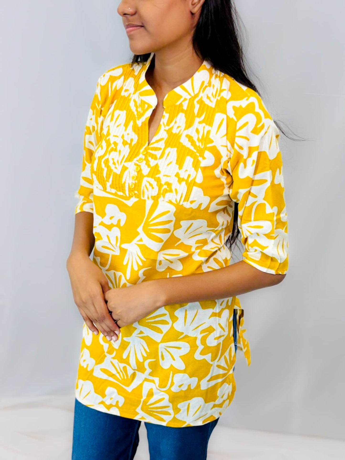 Woman wearing a yellow and white floral patterned shirt against a plain background