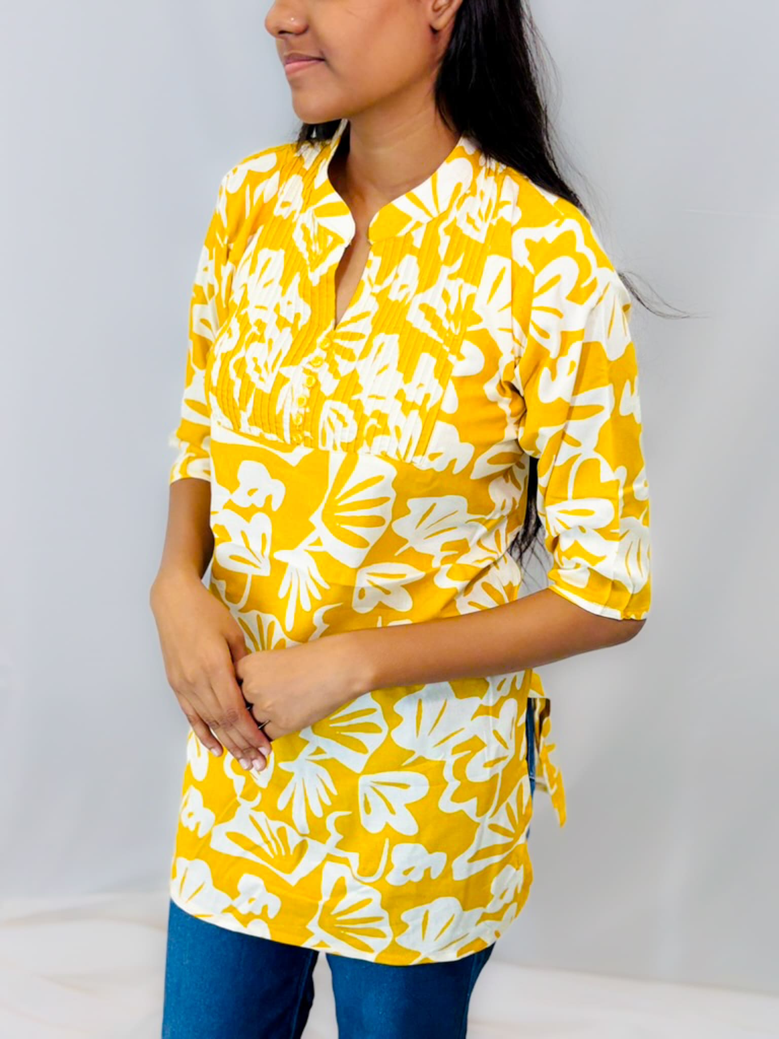 Woman wearing a yellow and white floral patterned shirt against a plain background
